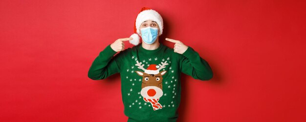 Concept de coronavirus du nouvel an et homme heureux de distanciation sociale en bonnet de Noel et chandail de Noël r...