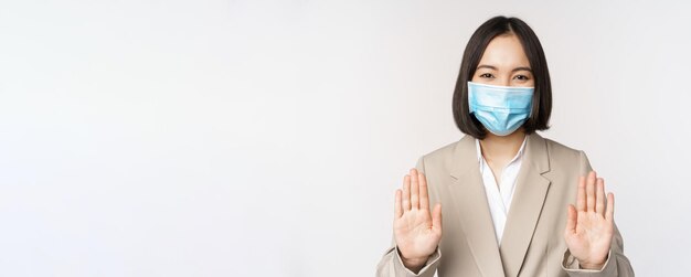 Concept de coronavirus et de travail Portrait d'une femme asiatique au bureau portant un masque médical et montrant un geste d'interdiction d'arrêt fond blanc