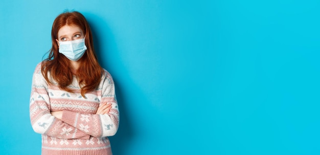 Photo gratuite concept de covid et de pandémie d'hiver adolescente rousse ignorante dans le masque facial roule les yeux et te regarde