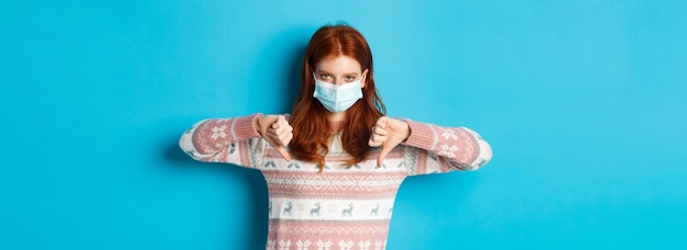 Photo gratuite concept de covid et de pandémie d'hiver bouleversé et en colère rousse en masque facial montrant le pouce de désapprobation