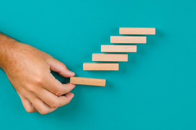 Concept de croissance d'entreprise sur table turquoise à plat. main empiler des blocs de bois.