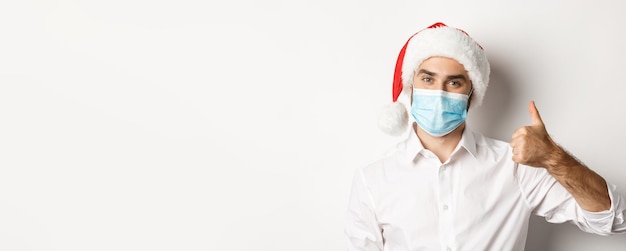 Concept de distanciation sociale covid et de vacances d'hiver homme satisfait en masque facial et spectacle de bonnet de noel