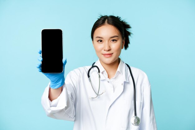 Concept de docteur en médecine Web souriant médecin asiatique montrant l'écran du téléphone portable debout dans la clinique un...