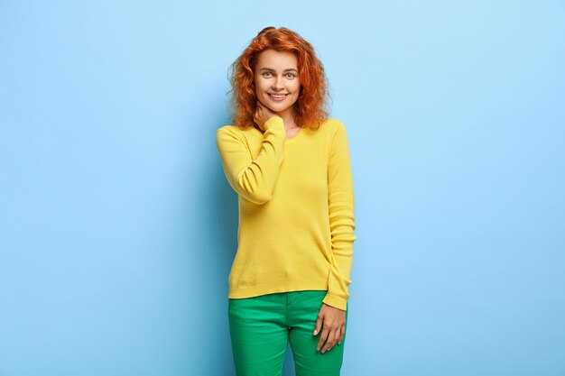 Concept d'émotions. Charmante belle femme rousse touche le cou et sourit agréablement à la caméra