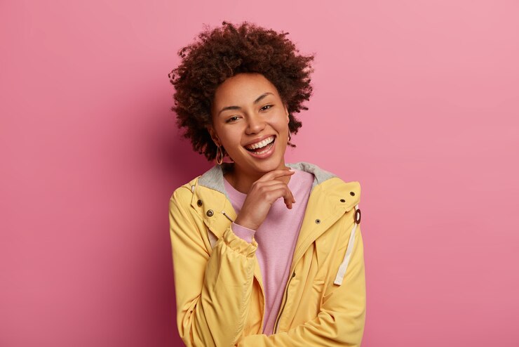 Photo gratuit concept d'émotions et d'expressions de visage. joyeuse femme optimiste avec une coiffure frisée, garde la main sous le menton, regarde avec joie, entend des nouvelles agréables