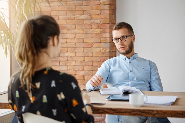 Concept d'entreprise. Une femme anonyme aux cheveux noirs assise à table dans un bureau devant un directeur des ressources humaines sérieux et mature, parlant des responsabilités professionnelles lors d'un entretien d'embauche.