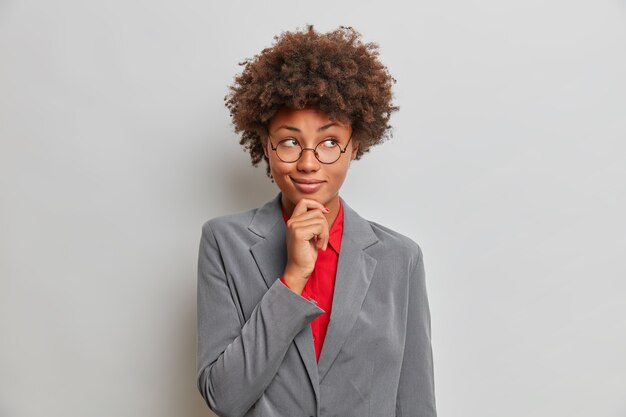 Concept d'entreprise. Une femme à la peau sombre et réfléchie tient le menton et détourne les yeux pensivement constitue un excellent plan