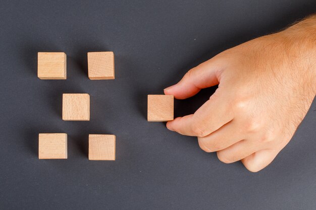 Concept d'entreprise sur table gris foncé à plat. main ramassant un cube en bois.