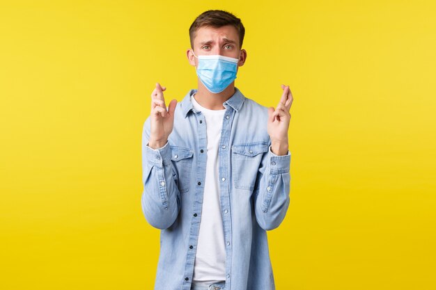 Concept d'épidémie de pandémie de covid-19, mode de vie pendant la distanciation sociale du coronavirus. Un gars désespéré et désespéré portant un masque médical, se sentant nerveux, croise les doigts, bonne chance, attendant des nouvelles importantes.