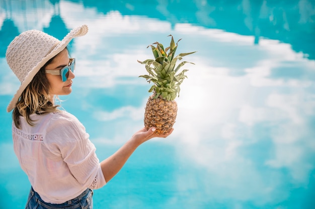 Concept d'été et de la piscine avec une femme tenant des ananas