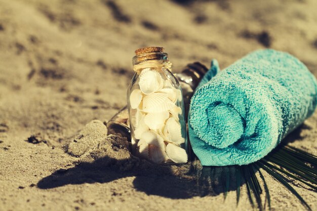 Concept d&#39;été ou de vacances. Coquillages en bouteilles sur sable avec une serviette bleue. Toning.