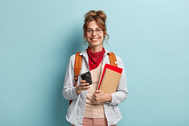 Concept d'étude, de loisirs et de style de vie. Une fille européenne a un sourire sincère, revient de l'université de bonne humeur, boit du café