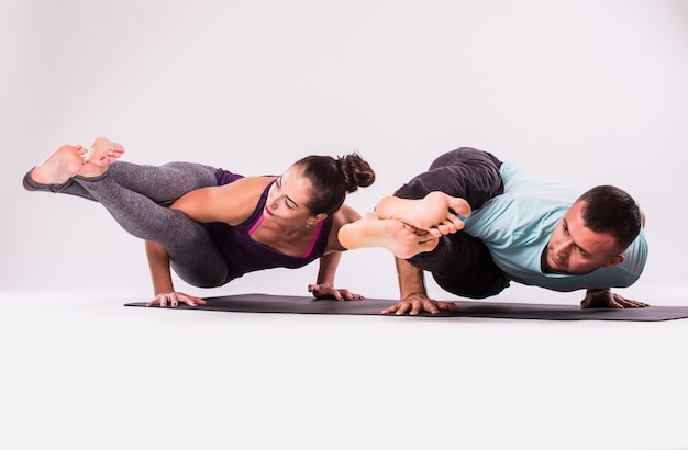 Photo gratuite concept d'exercices de yoga. jeune couple en bonne santé en position d'yoga sur fond blanc