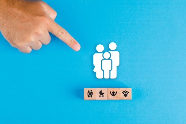Concept de famille avec bloc en bois, icône de famille de papier sur table bleue à plat. main de l'homme pointant.