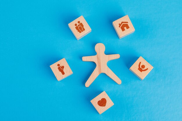 Concept de famille avec des icônes sur des cubes en bois, figure humaine sur table bleue à plat.