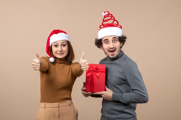 Concept festif de nouvel an humeur avec drôle satisfait heureux joli couple portant des chapeaux de père Noël rouge sur fond gris