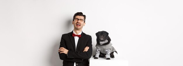 Photo gratuite concept de fête et de célébration des animaux triste propriétaire de chien pleurant portant un costume debout près d'un mignon carlin noir