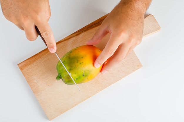 Photo gratuite concept de fruits à plat. mains coupant la papaye sur planche de bois.