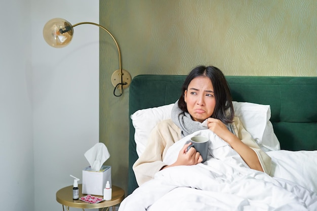 Photo gratuite concept de grippe et de vaccination covid fille coréenne allongée dans son lit avec la grippe attrapant le froid buvant chaud