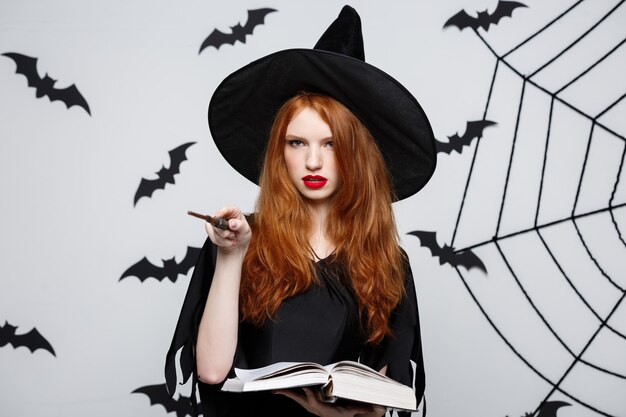 Concept d'Halloween - Belle sorcière jouant avec un bâton magique sur un mur gris.