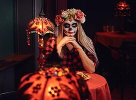 Photo gratuite concept d'halloween et de muertos. jeune fille blonde avec un maquillage mort-vivant dans une couronne de fleurs mangeant des nachos dans un restaurant mexicain.