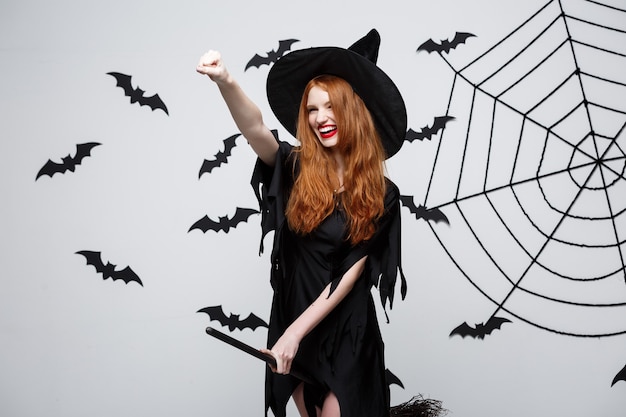 Photo gratuite concept d'halloween, une sorcière élégante et heureuse aime jouer avec un manche à balai