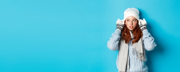 Photo gratuite concept d'hiver et de vacances jolie fille rousse qui sort à l'extérieur enfiler un bonnet et des gants en regardant à gauche st