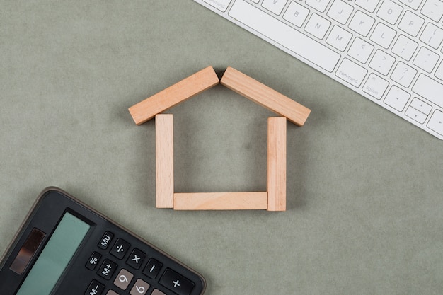 Concept immobilier avec des blocs de bois, calculatrice, clavier sur fond plat gris.