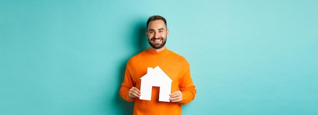 Concept immobilier heureux jeune homme à la recherche d'un loyer de maison tenant un papier de maison et souriant st