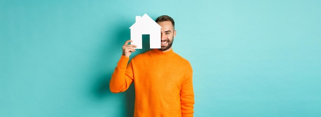 Photo gratuite concept immobilier heureux jeune homme à la recherche d'un loyer de maison tenant un papier de maison et souriant st