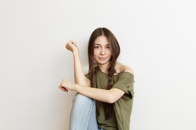 Concept de jeunesse, de personnes, de loisirs et de style de vie. Tendre jeune femme européenne insouciante avec une coiffure en désordre sauvage se sentant détendue, passant une journée à la maison, assise seule dans sa chambre, habillée avec désinvolture