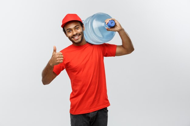 Concept de livraison - Handsome African American Delivery Man tenant un réservoir d&#39;eau. Isolé sur fond de studio gris. Espace de copie.