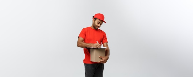 Concept de livraison Portrait d'un beau livreur afro-américain ou d'un coursier écrivant sur un document de commande isolé sur fond gris studio espace de copie