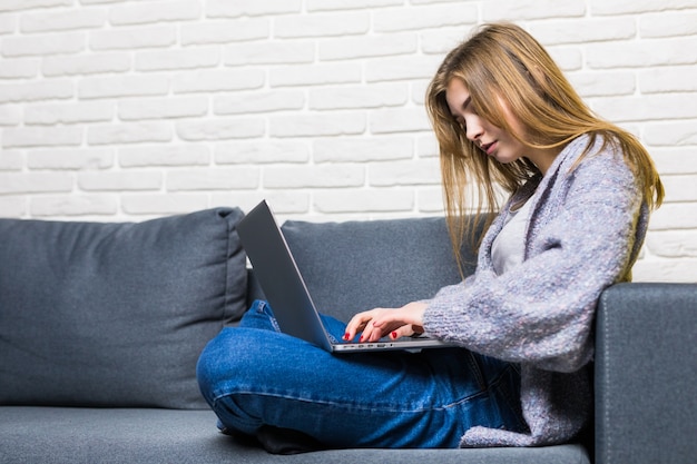 Concept de maison, technologie et internet - adolescente occupée allongée sur le canapé avec un ordinateur portable à la maison