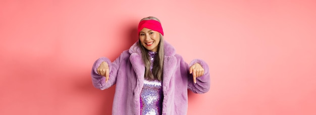 Photo gratuite concept de mode et de shopping femme asiatique senior souriante pointant les doigts vers le bas montrant la publicité du magasin