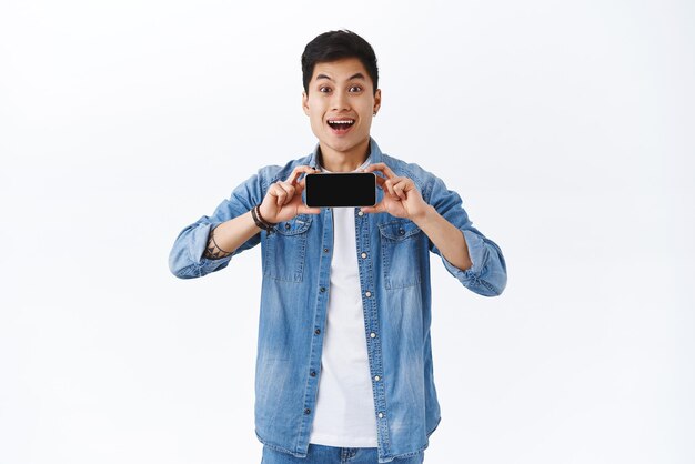 Concept de mode de vie en ligne technologique Regardez cet homme asiatique souriant, étonné et excité, montrant un écran de téléphone portable se vantant du score le plus élevé dans l'application ou le jeu sur fond blanc