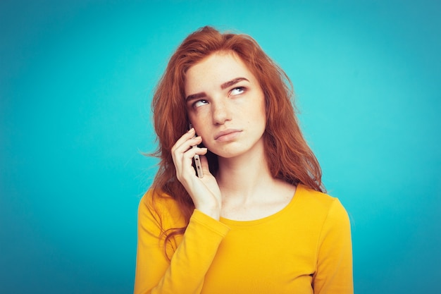 Concept de mode de vie - Portrait de ginger red hair girl avec une expression étonnante et stressante tout en parlant avec un ami par téléphone portable. Isolé sur fond bleu pastel. Espace de copie.