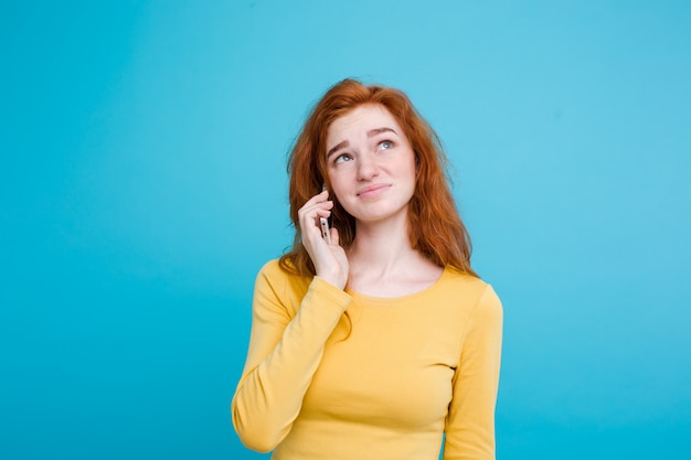 Concept de mode de vie - Portrait de ginger red hair girl avec une expression étonnante et stressante tout en parlant avec un ami par téléphone portable. Isolé sur fond bleu pastel. Espace de copie.