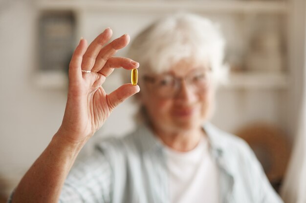 Concept de nourriture, nutrition, régime et santé. Gros plan de la main d'une femme âgée tenant de l'huile de poisson ou un supplément d'acide gras polyinsaturé oméga-3 en forme de capsule, va prendre un pendant le déjeuner