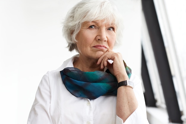 Concept de personnes, âge, maturité et mode de vie. Portrait de femme d'affaires mature sérieuse élégante avec des cheveux blancs courts touchant le menton, ayant un regard pensif, pensant aux idées et plans d'affaires