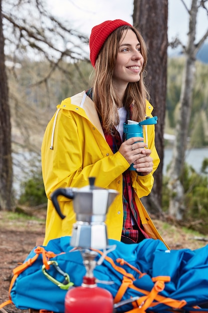 Concept de personnes et de camping. Une voyageuse satisfaite boit une boisson chaude dans un thermos après une randonnée