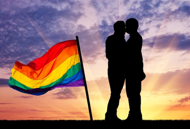 Concept de personnes homosexuelles. silhouette joyeux gay s'embrassant contre le ciel du soir et un drapeau arc-en-ciel