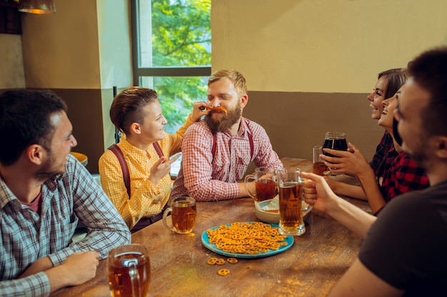 Concept de personnes, de loisirs, d'amitié et de communication - amis heureux, boire de la bière, parler et tinter des verres au bar ou au pub