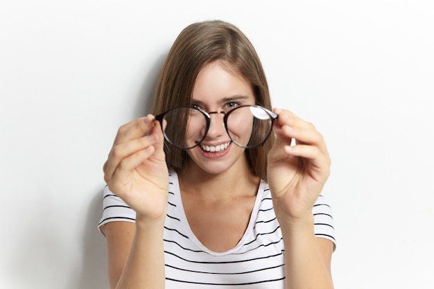 Concept de personnes, mode de vie, santé, lunettes, optique et vision. Portrait de jeune femme joyeuse heureuse tenant des lunettes élégantes