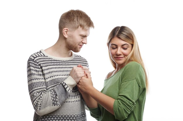 Concept de personnes, de relations et de romance. Séduisante jeune homme mal rasé avouant son amour à jolie fille mignonne tout en tenant ses deux mains, femme regardant vers le bas avec une expression timide, rougissant