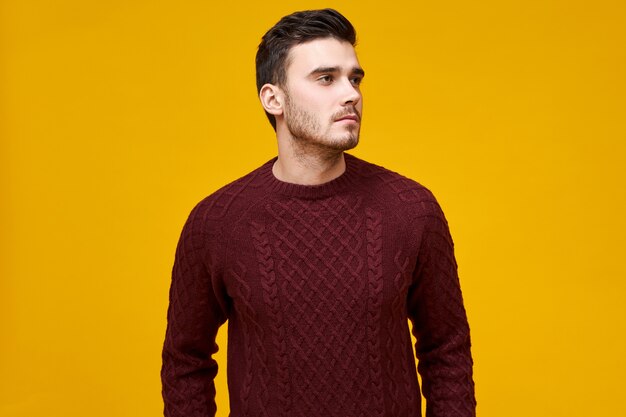 Concept de personnes, de style, de mode et de saison. Photo de jeune homme à la mode avec des poils et une coiffure élégante ayant une expression faciale sérieuse, regardant loin contre le mur de l'espace de copie