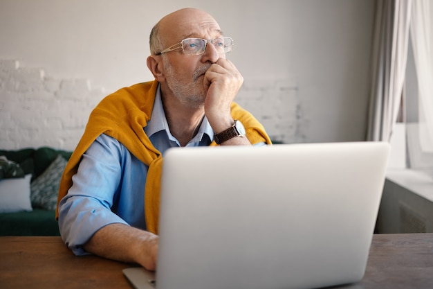 Concept de personnes, style de vie, technologie moderne, âge, entreprise, emploi et profession. Tir intérieur de bel homme barbu de race blanche écrivain tapant l'article pour son blog, à l'aide d'un ordinateur portable, ayant le visage de rêve