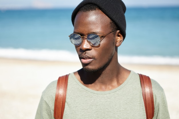 Concept de personnes, de style de vie, de voyage et d'aventure. Gros plan de séduisante jeune touriste afro-américaine avec sac à dos, ayant une belle promenade le long de la mer