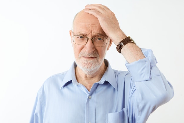 Concept de personnes, de vieillissement et de problèmes de santé. Frustré malheureux vieux caucasien homme avec barbe grise tenant la main sur sa tête chauve ayant une expression faciale oublieuse, souffrant de perte de mémoire