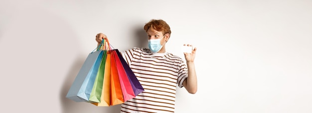 Photo gratuite le concept de quarantaine et de style de vie de covid a étonné un homme roux regardant des sacs à provisions après avoir acheté avec